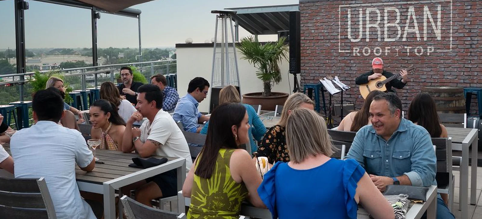 The rooftop at URBAN Eat.Drink in downtown Round Rock, with diners at tables and a guitarist playing under the Urban Rooftop sign