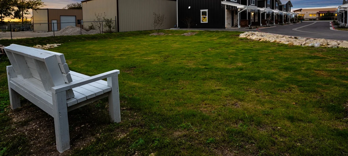 The fenced dog park at 20 Tate Lane: an open lawn with a bench, the homes and their lit porches beyond